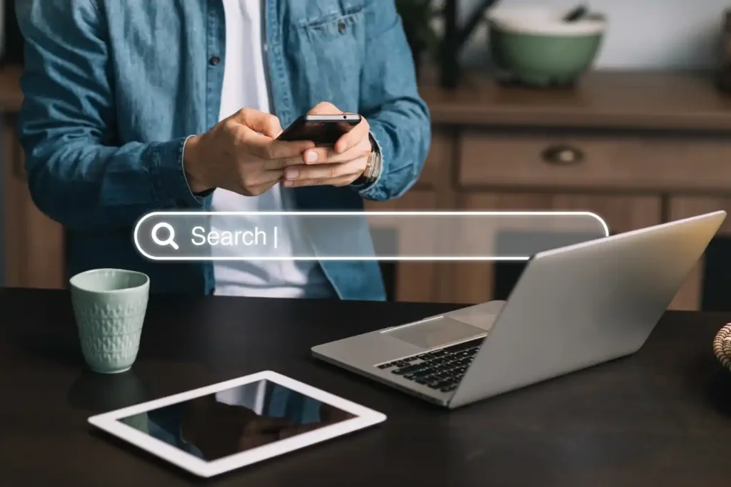 Persona utilizando un teléfono móvil frente a una laptop y una tablet, simbolizando la búsqueda de mejorar la visibilidad digital.