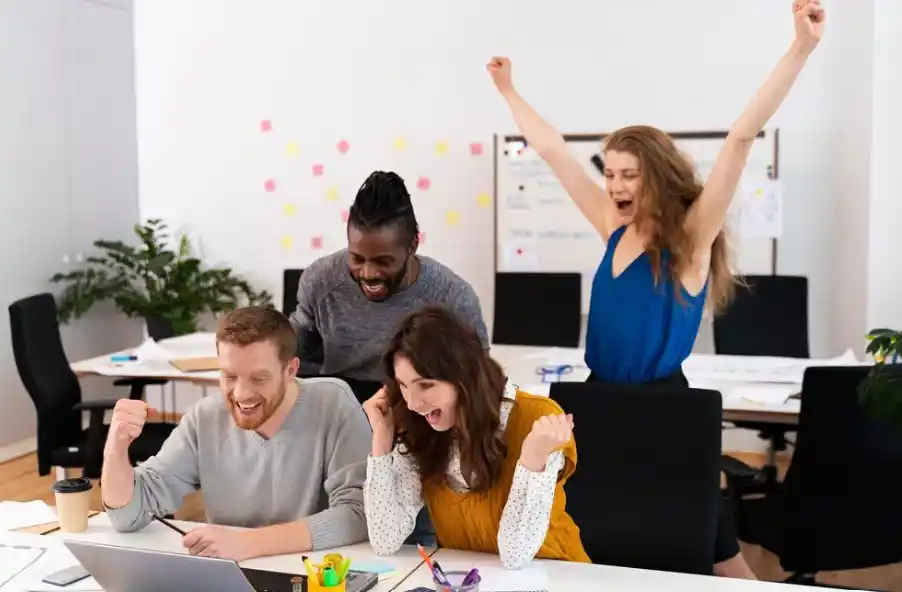 Equipo celebrando el éxito de una campaña publicitaria exitosa con SEO frente a una laptop en una oficina.