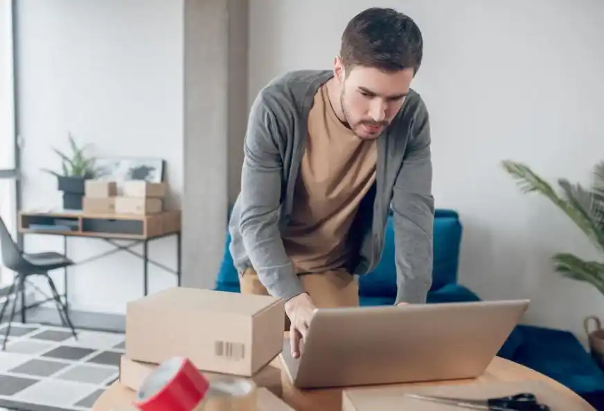 Emprendedor gestionando su negocio en línea desde una laptop, rodeado de cajas de envío, enfocándose en mejorar la visibilidad digital de su PYME.