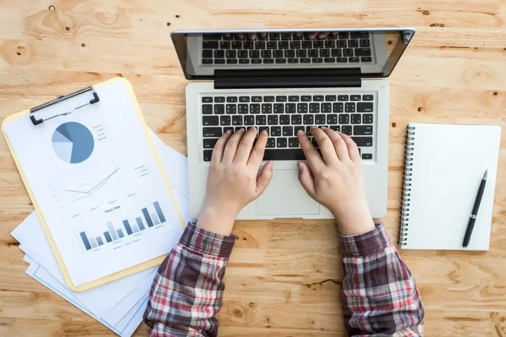 Vista superior de una persona usando un portátil en un escritorio de madera evaluando estrategias seo y sem