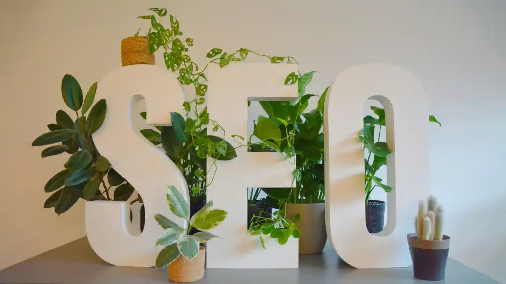 Letras grandes “SEO” rodeadas de plantas verdes, simbolizando el crecimiento y sostenibilidad del posicionamiento en buscadores