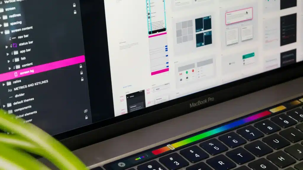 Pantalla de MacBook con editor de diseño UI mostrando elementos visuales y componentes de una app móvil